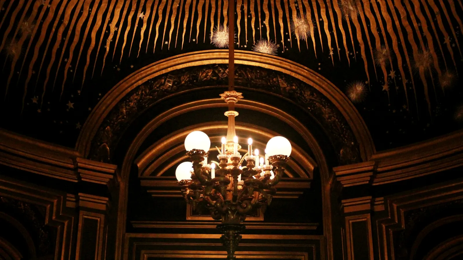 A gilded chandelier beneath an arched, star-painted ceiling